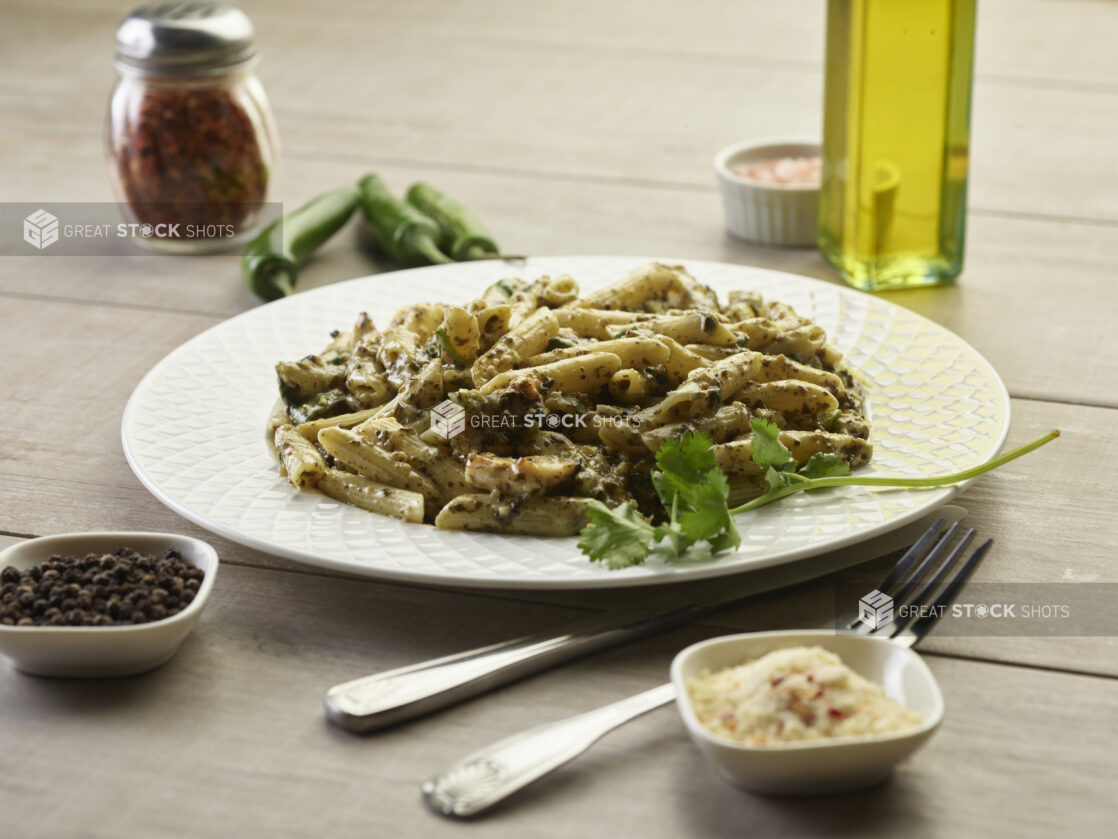 White bowl of pistachio pesto pasta with chicken surrounded by seasonings