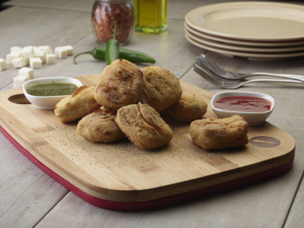 Order of paneer pakoras on a wooden board with two dipping sauces