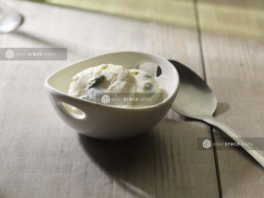 Bowl of rasgulla topped with pistachios on a wooden background with a spoon