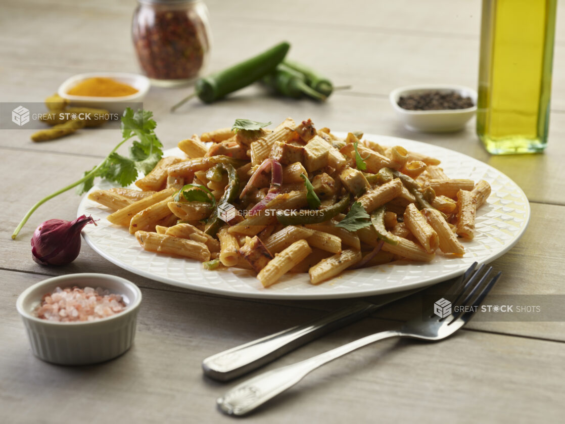 Palak Paneer pasta with peppers and red onions in a white bowl surrounded by ingredients on a wooden table