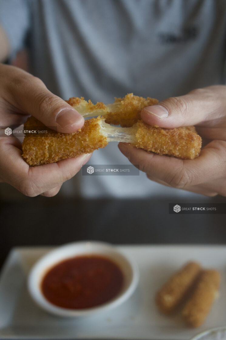 Man pulling apart cheese sticks with long cheese strands