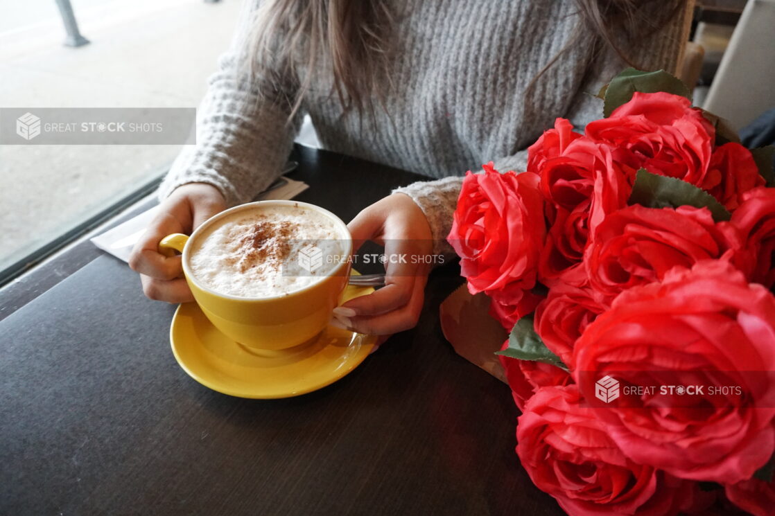 Woman in a cafe with a cappuccino and a bouquet of red roses