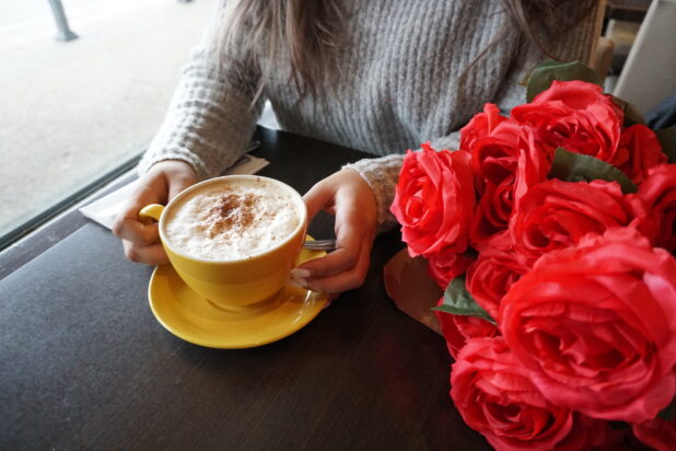 Woman in a cafe with a cappuccino and a bouquet of red roses