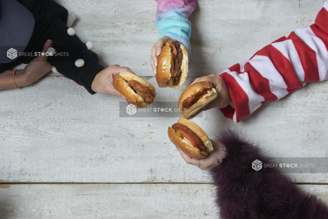 Different unique arms holding out hamburgers and chicken sandwiches over a wood table