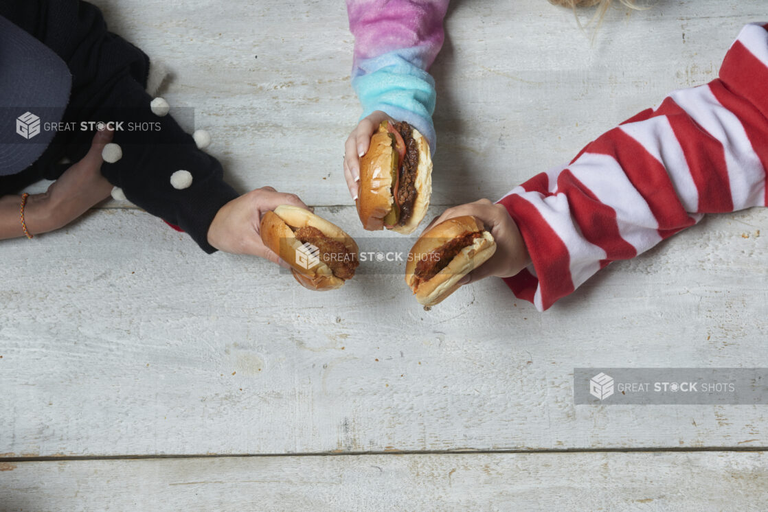 Different unique arms holding out hamburgers and chicken sandwiches over a wood table