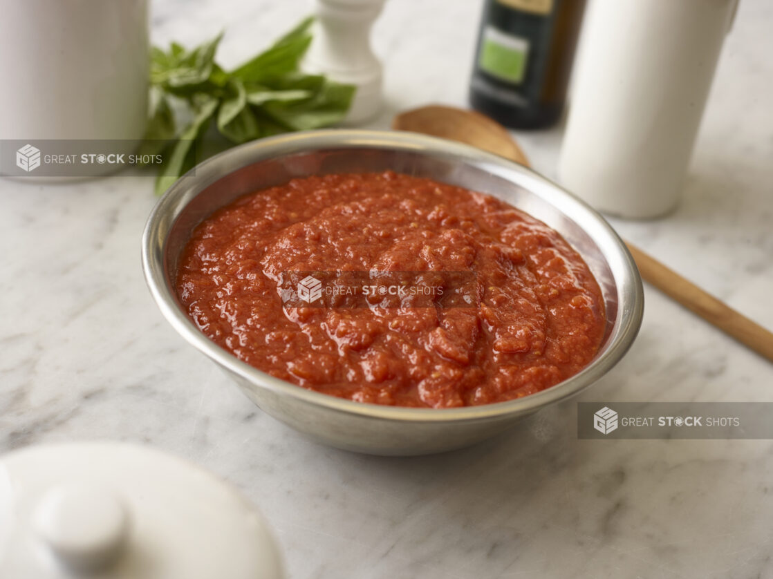 Large metal bowl of fresh tomato sauce on a white marble background