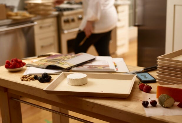 Chef preparing a wooden catering tray with cheese, fruit and nuts in a kitchen