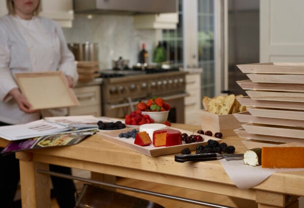 Chef holding a wooden tray while preparing a wooden catering tray with cheese and fruit in a kitchen