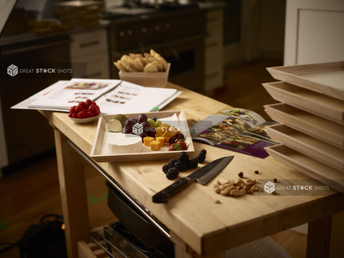 Preparing a wooden catering tray with cheese and fruit in a kitchen with instructions on a wooden table