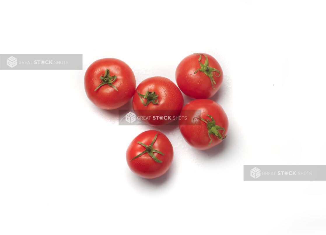 Five whole hothouse tomatoes with the pedicel and sepal showing on a white background