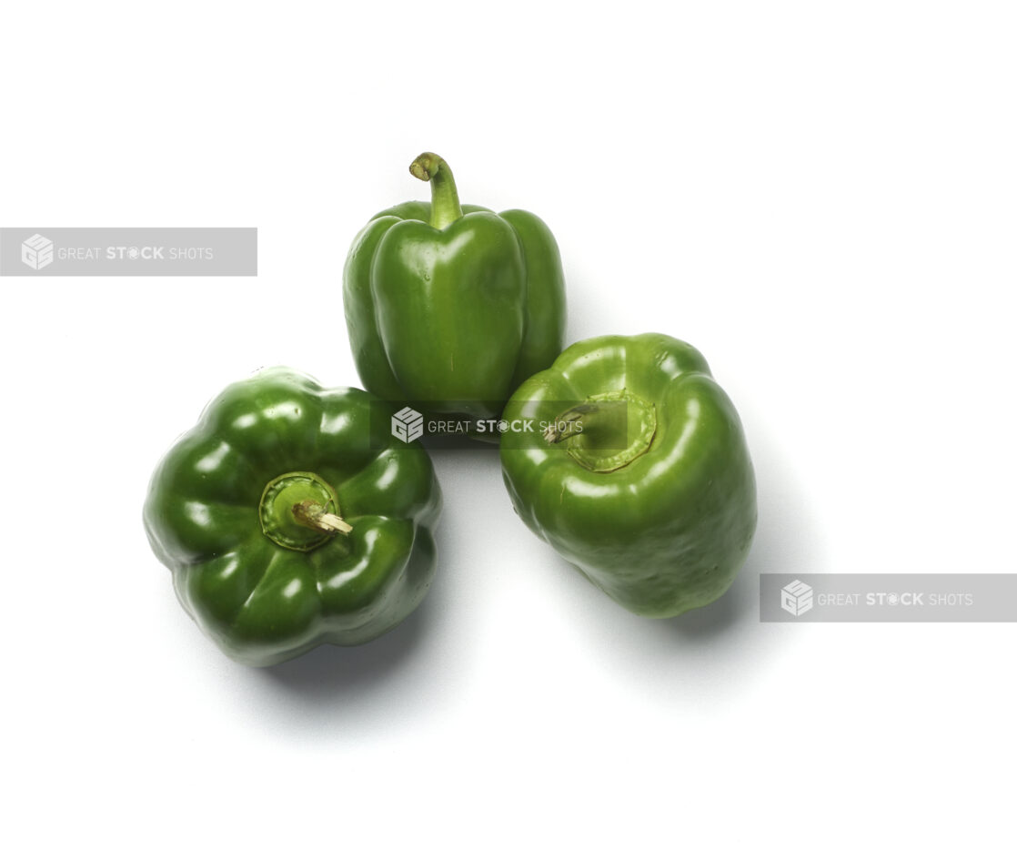 Three whole green bell peppers tilted on different angles on a white background