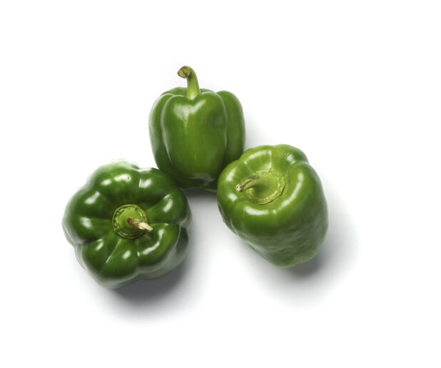 Three whole green bell peppers tilted on different angles on a white background
