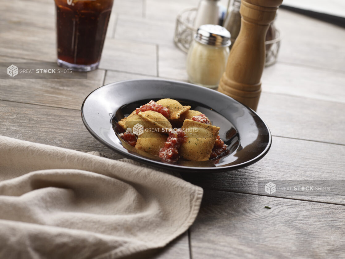 Deep fried ravioli with and tomato sauce in a round black bowl on a grey wooden background