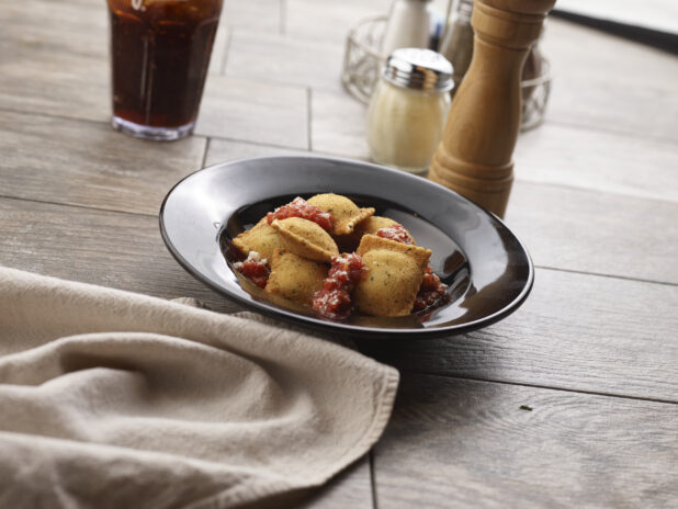 Deep fried ravioli with and tomato sauce in a round black bowl on a grey wooden background