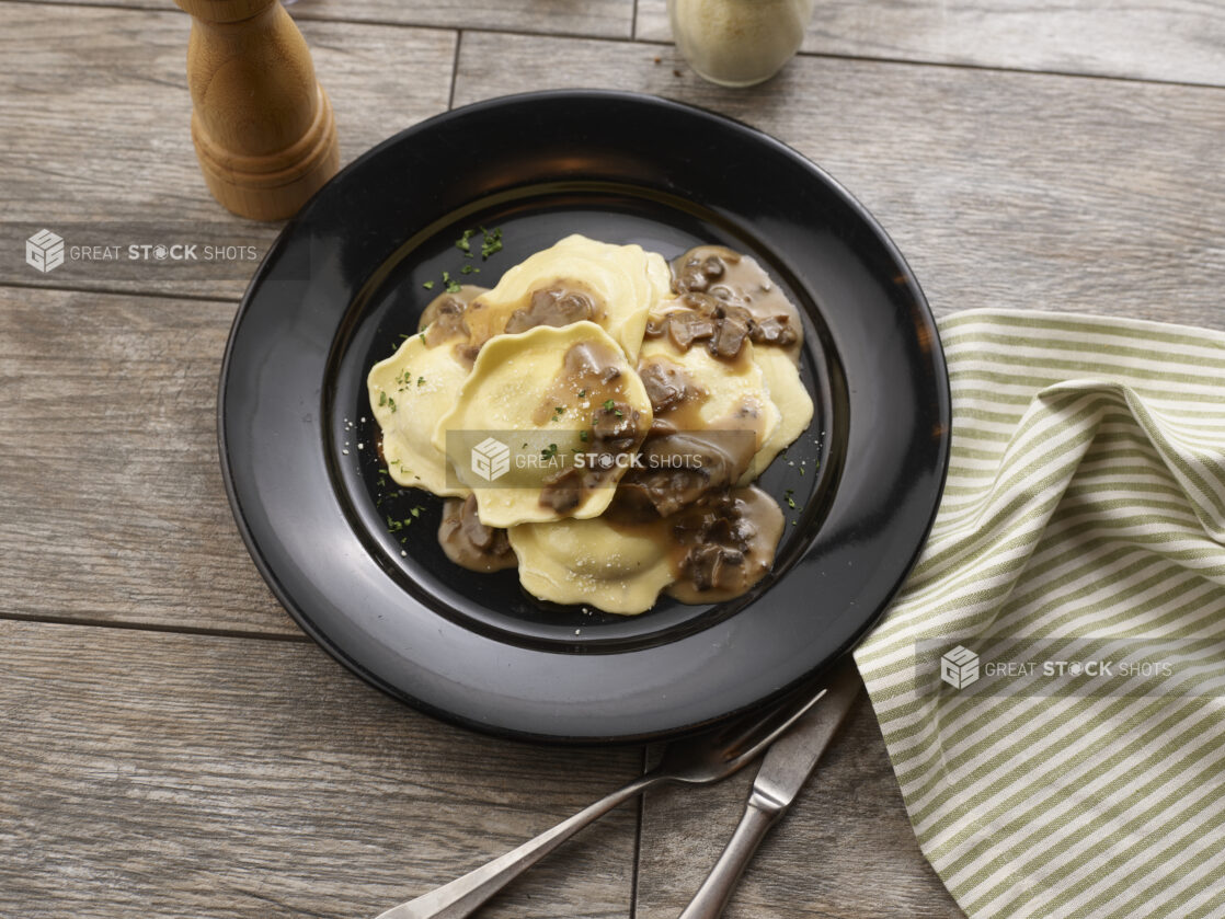 Mezzalune ravioli with mushroom sauce in a round black bowl on a grey wooden background, overhead