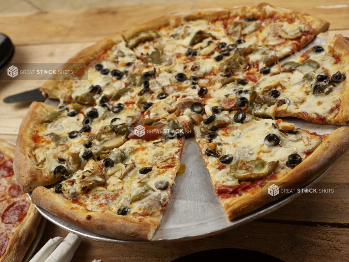 Whole 3 topping pizza, sliced, with black olives, roasted peppers and mushrooms on a wooden background