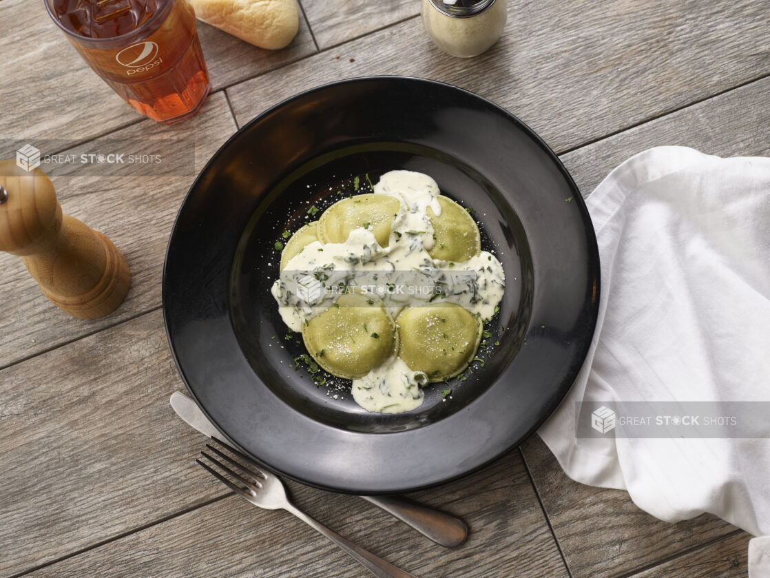 Mezzalune ravioli with cream sauce in a black pasta bowl on a grey wooden background, overhead view