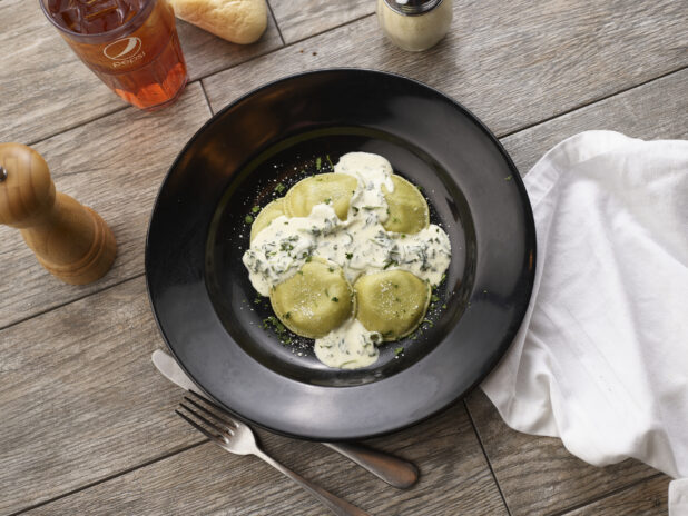 Mezzalune ravioli with cream sauce in a black pasta bowl on a grey wooden background, overhead view