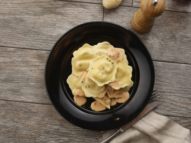 Ravioli with rose sauce in a black pasta bowl on a grey wooden background, overhead view