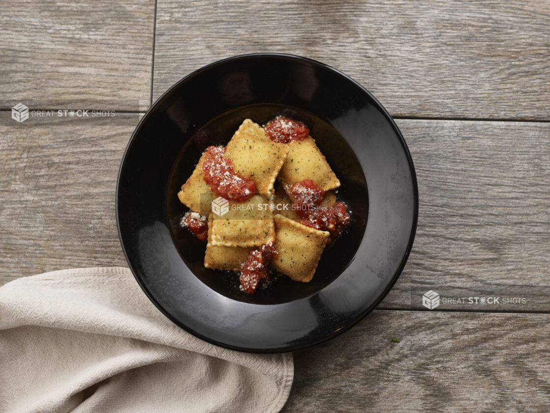 Deep fried ravioli with tomato sauce in a round black bowl on a grey wooden background, overhead view