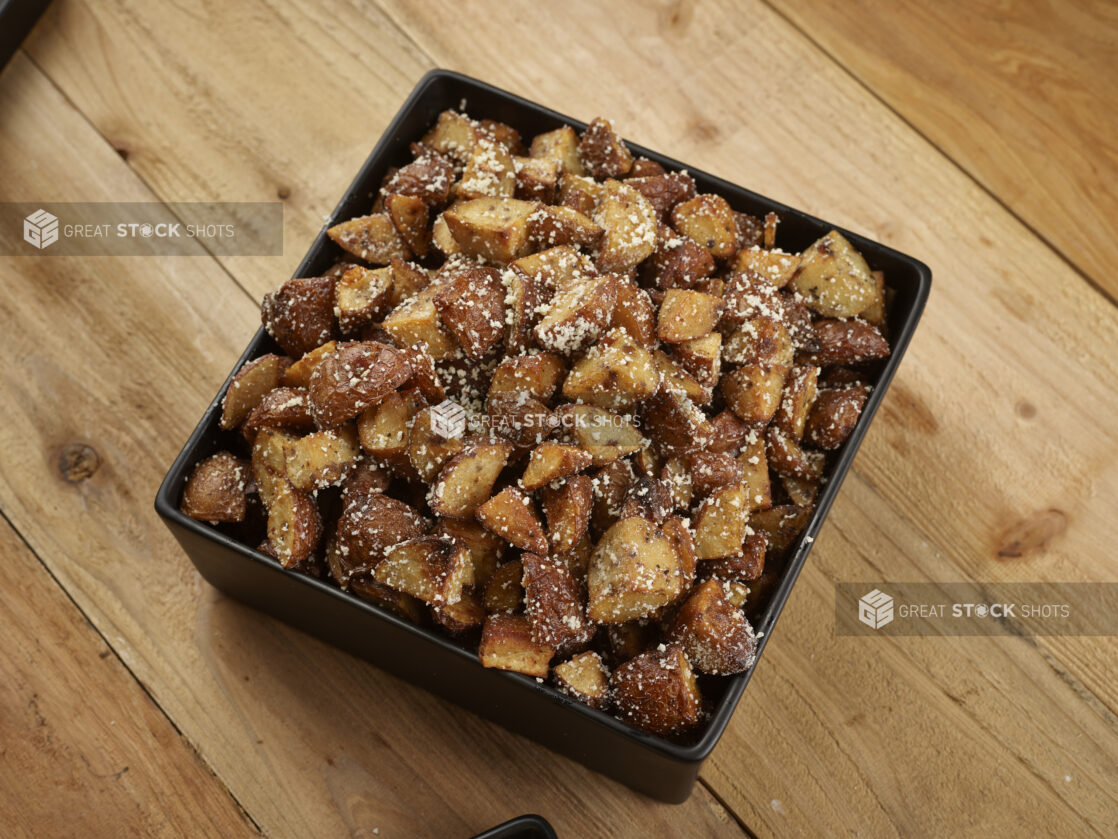 Roasted parmesan potatoes in a square black bowl on a wooden background