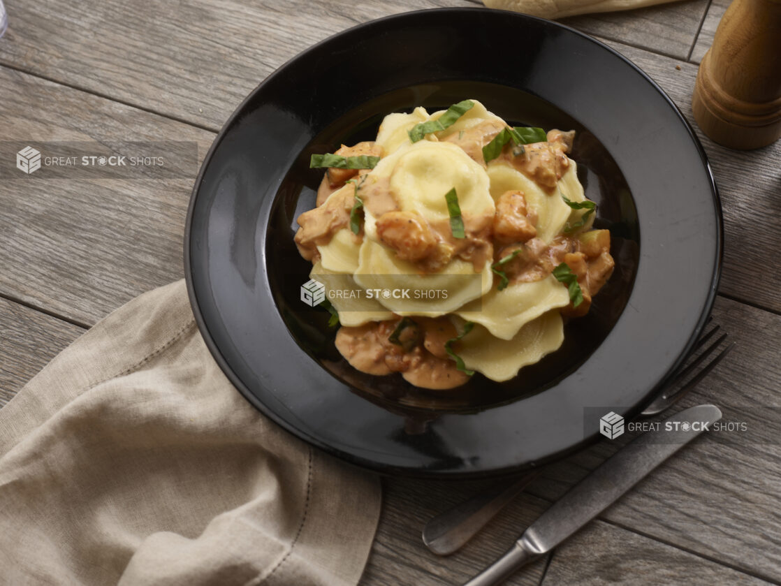 Mezzalune ravioli with rose sauce and fresh chopped basil in a black pasta bowl on a grey wooden background