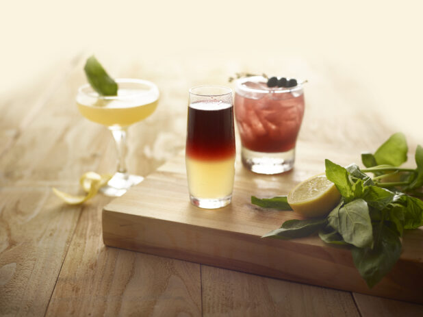 Cocktails with sliced lemon and fresh basil on a wooden board, on a wooden background
