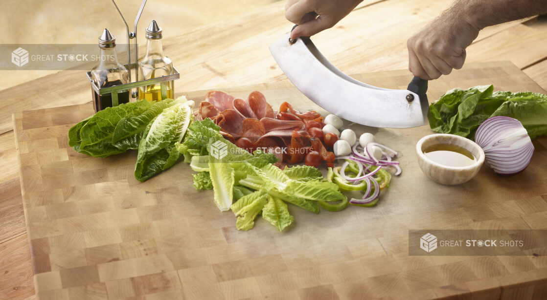 Chopped salad with fresh romaine, bocconcini cheese, red onion, tomatoes and Italian meats with olive oil and balsamic vinegar all on a wooden background