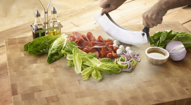 Chopped salad with fresh romaine, bocconcini cheese, red onion, tomatoes and Italian meats with olive oil and balsamic vinegar all on a wooden background