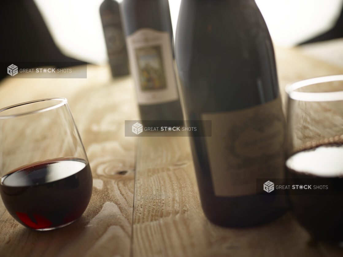 Bottles of red wine and stemless wine glasses with red wine on an unfinished wooden tabletop