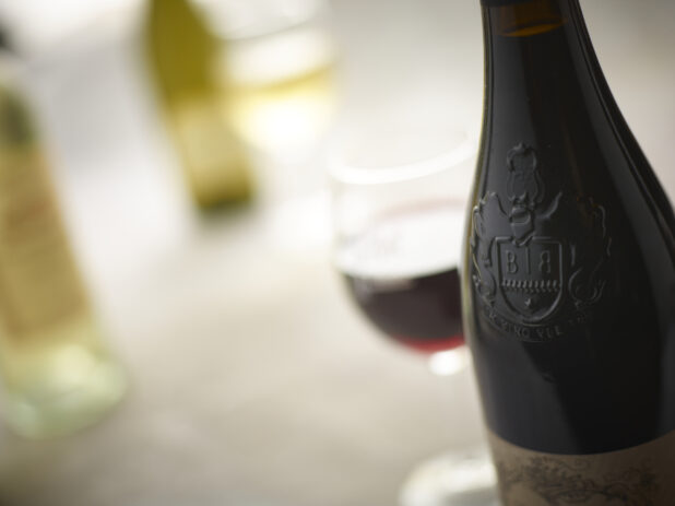 Up close view of a red wine bottle with a glass of red wine, glass of white wine and white wine bottles in the background