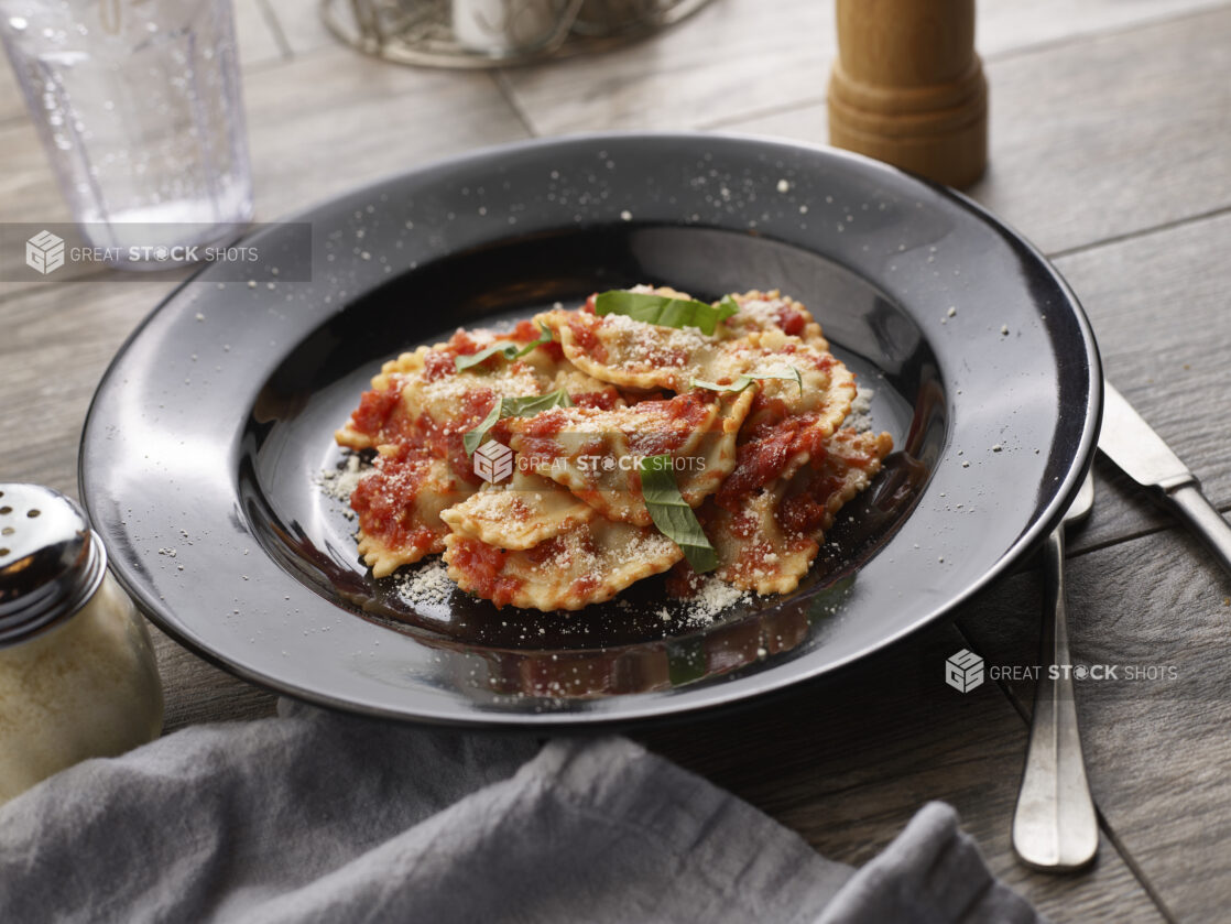 Agnolotti with tomato sauce and fresh basil in a black pasta bowl on a grey wooden background