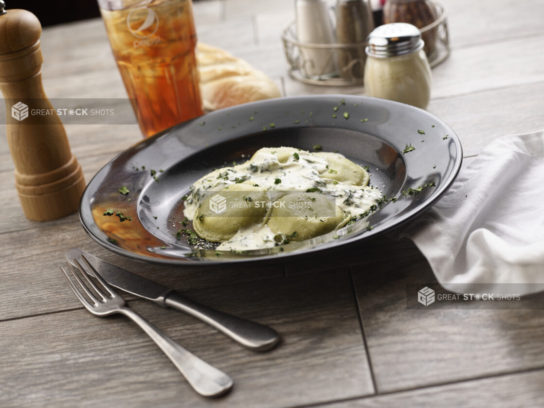 Mezzalune ravioli with cream sauce in a black pasta bowl on a grey wooden background