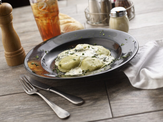 Mezzalune ravioli with cream sauce in a black pasta bowl on a grey wooden background