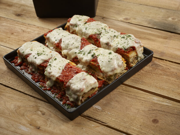 Lasagna, beautifully displayed, on a square black platter on a wooden background