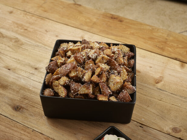 Roasted parmesan potatoes in a square black bowl on a wooden background