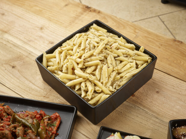Penne pasta with olive oil and seasoning in a square black bowl on a wooden background