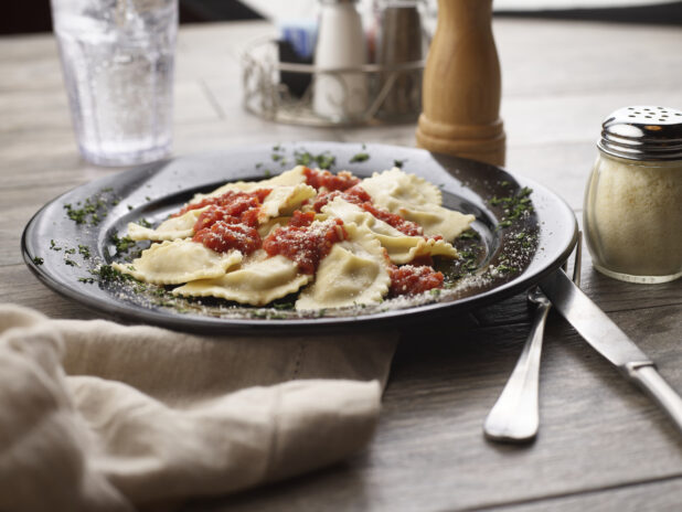 Agnolotti with tomato sauce and parmesan in a black bowl on a grey wooden background