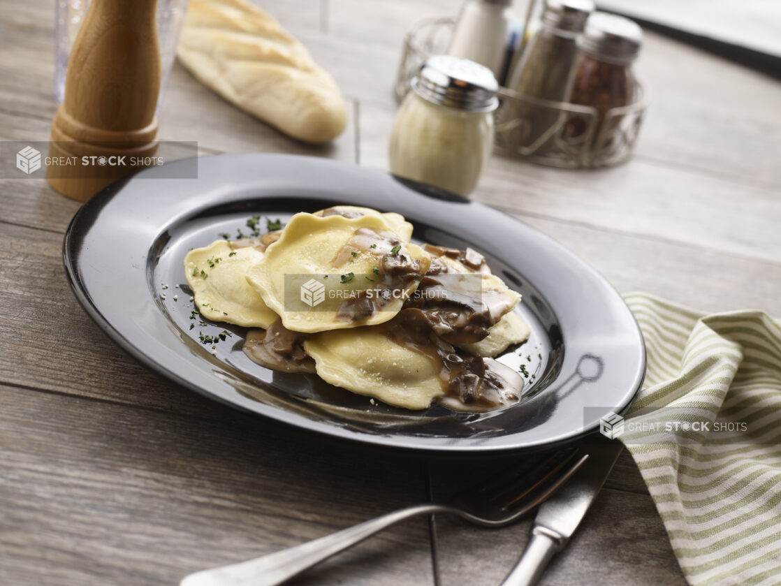 Mezzalune ravioli with mushroom sauce in a black pasta bowl on a grey wooden background