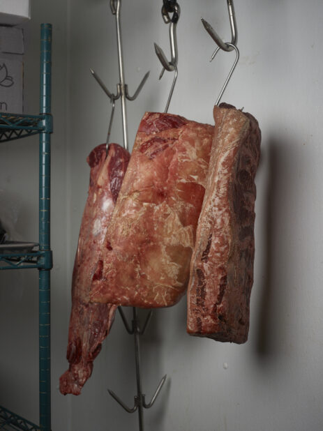 3 sides of beef hooked and hanging in a fridge
