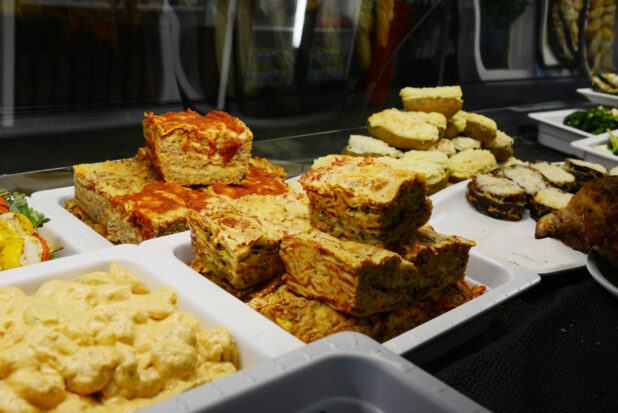 Various takeout dinner items in a restaurant/store display case - lasagna, stuffed baked potatoes, eggplant parmesan, and others