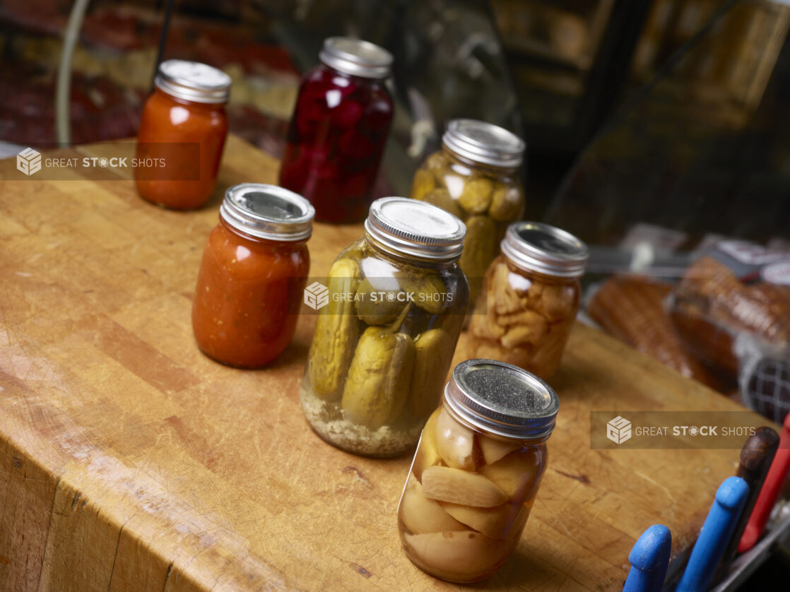 Various jars of pickled/preserved vegetables, fruit and sauces on a butchers block table on a 45 degree angle