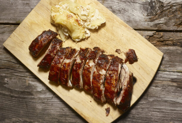 Full rack of BBQ ribs with a side of scalloped potatoes on a wooden cutting board on a rustic wooden background