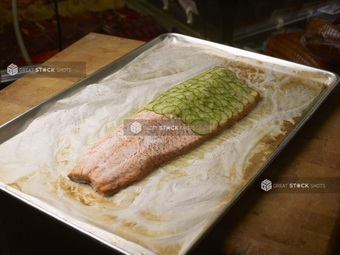 Whole cooked salmon with cucumber slices on half on a sheet pan on a butcher's block