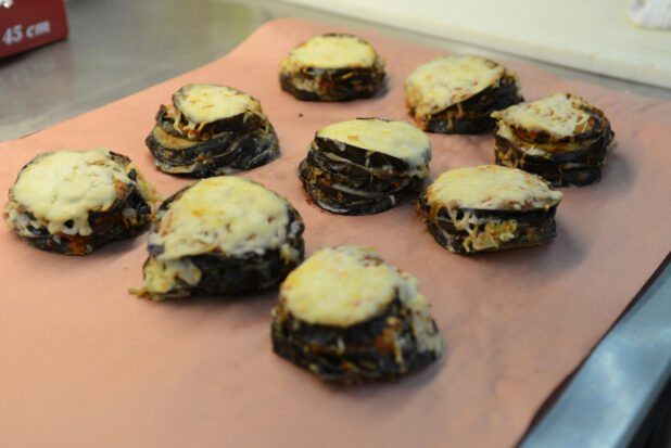 Stacked eggplant parmesans on butcher's paper on a stainless steel table