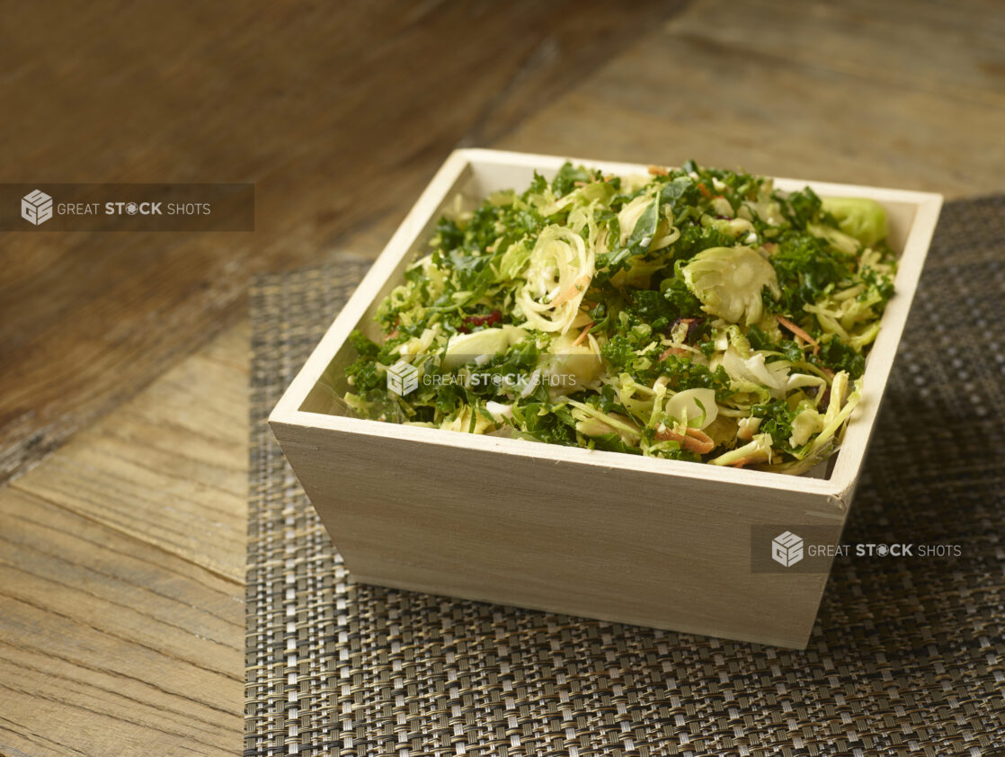 Rustic kale and brussels sprouts salad in a wood catering box on a wooden background