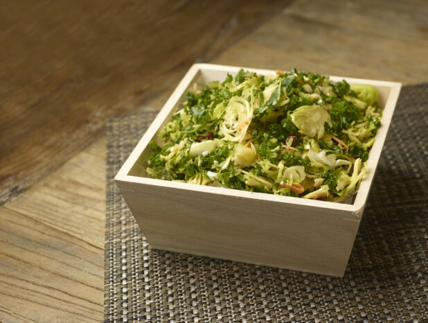 Rustic kale and brussels sprouts salad in a wood catering box on a wooden background