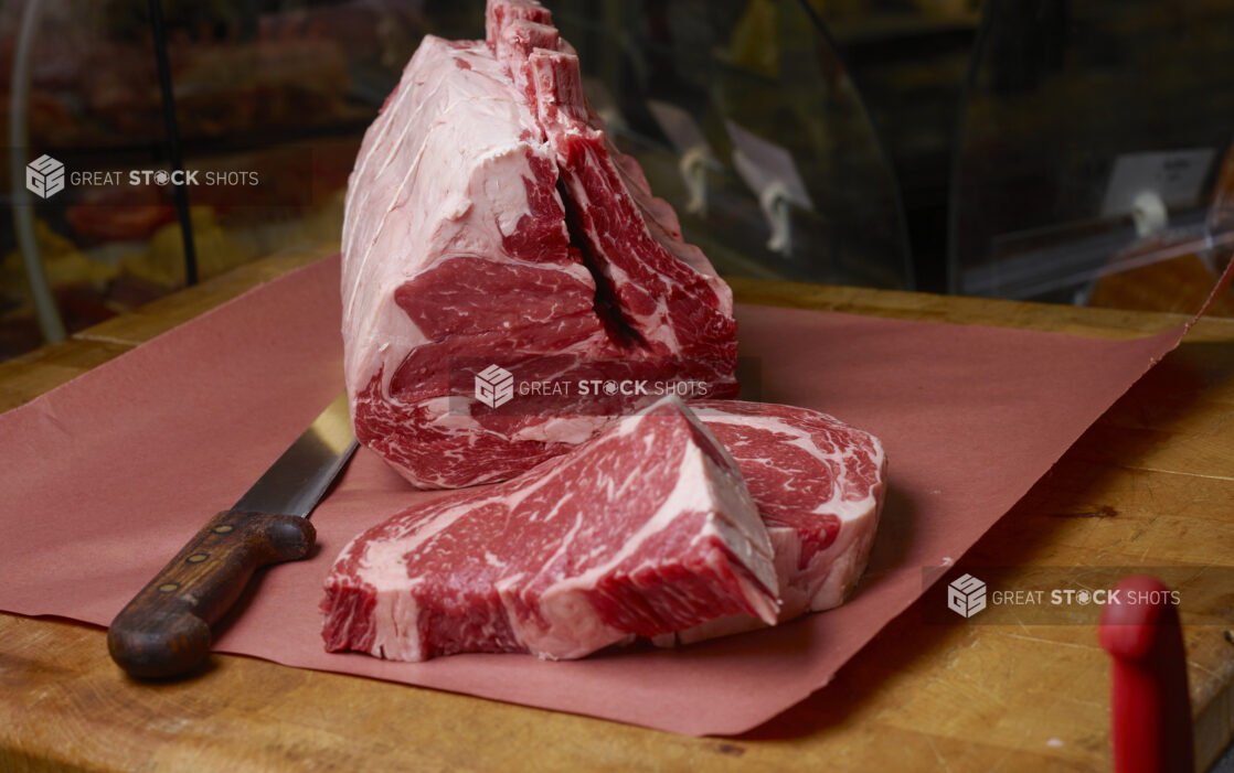 Uncooked prime rib roast with slices of prime rib on butchers paper on a butchers block with a boning knife