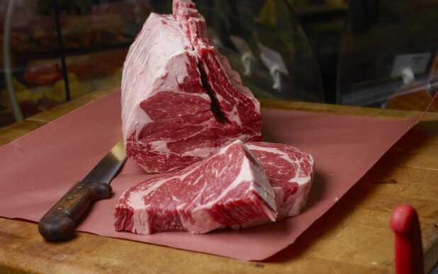 Uncooked prime rib roast with slices of prime rib on butchers paper on a butchers block with a boning knife