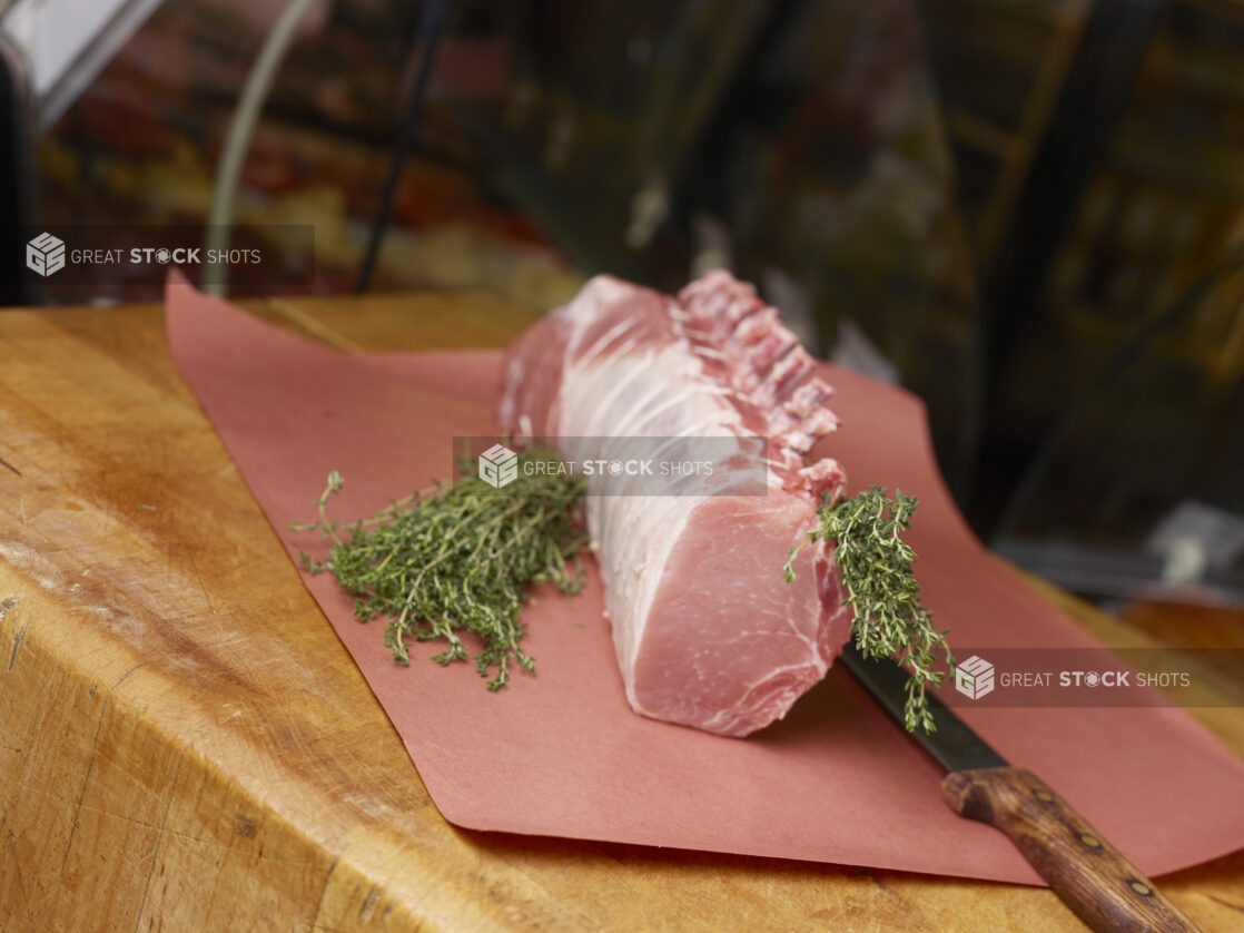 Whole pork rib rack roast, uncooked, on butchers paper with fresh thyme and a boning knife on a butchers block